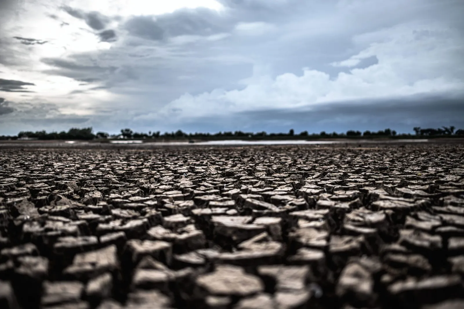 Ausgetrockneter, tief aufgerissener Boden unter dunklen Wolken