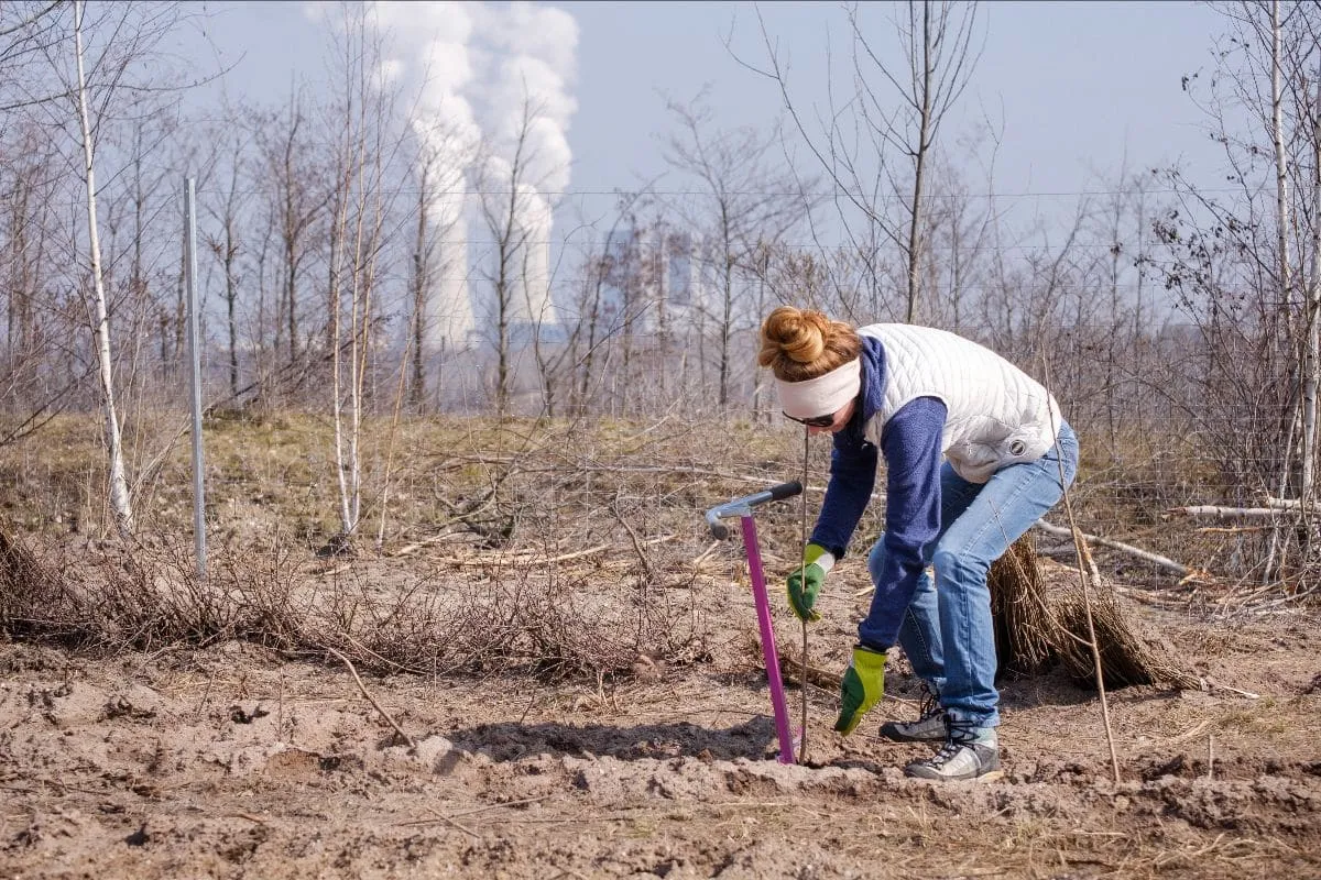Ruth von Heusinger, Gründerin von ForTomorrow, pflanzt einen Baum, im Hintergrund Kühltürme