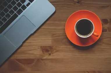 Laptop und eine Tasse Kaffee auf einem Holztisch, von oben fotografiert