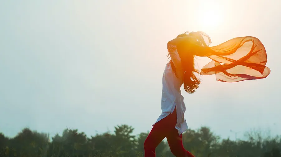 Silhouette einer Frau mit wehendem Schal im Gegenlicht der Sonne
