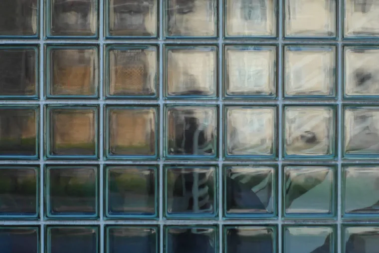 Fassade aus Glasbausteinen mit verschwommenen Reflexionen und Schattenumriss einer Person dahinter
